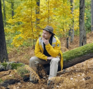 colin novick sitting on a downed tree in a colorful forest