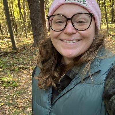 ashley hoffman smiling in woods with hat and green vest