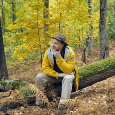 colin novick sitting on a downed tree in a colorful forest